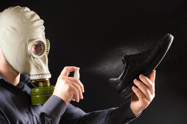 Un uomo con una maschera antigas tratta le sue scarpe con uno spray profumato