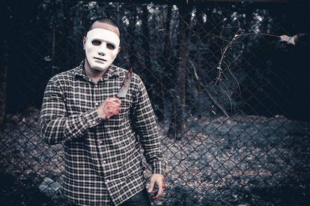 Un uomo con una maschera bianca si trova davanti a un recinto.