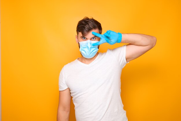 Un uomo con una maschera medica ha presentato la sua mano e mostra 2 dita vicino al suo occhio.