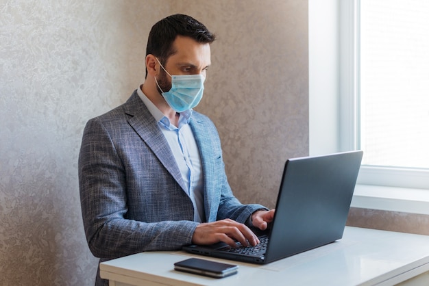 Un uomo con una maschera medica lavora su un laptop