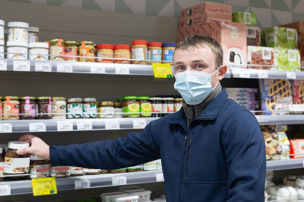 Un uomo con una maschera protettiva sceglie i prodotti nel negozio Alimenti e bevande Generi alimentari