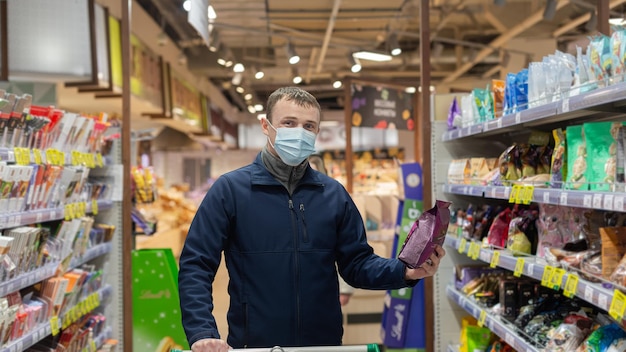 Un uomo con una maschera protettiva sceglie i prodotti nel negozio Generi alimentari Cibo e bevande