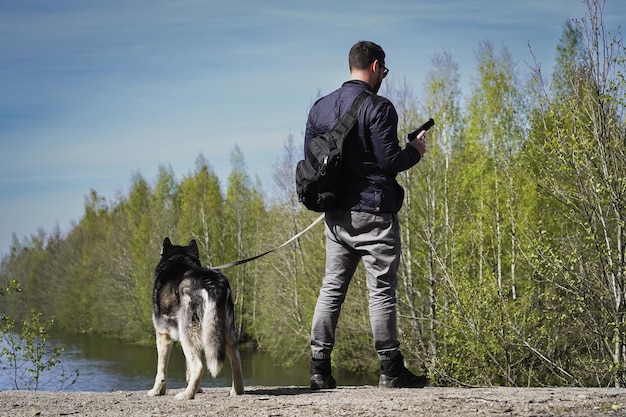 Un uomo con una pistola in mano con un cane al guinzaglio vicino a uno stagno in natura