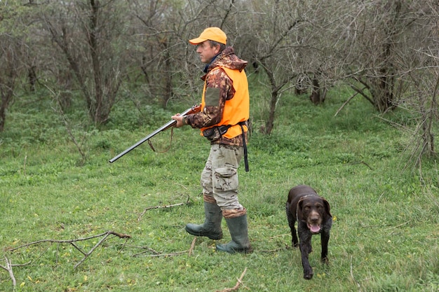 Un uomo con una pistola in mano e un giubbotto arancione a caccia di fagiani in una zona boscosa con tempo nuvoloso Cacciatore con cani in cerca di selvaggina