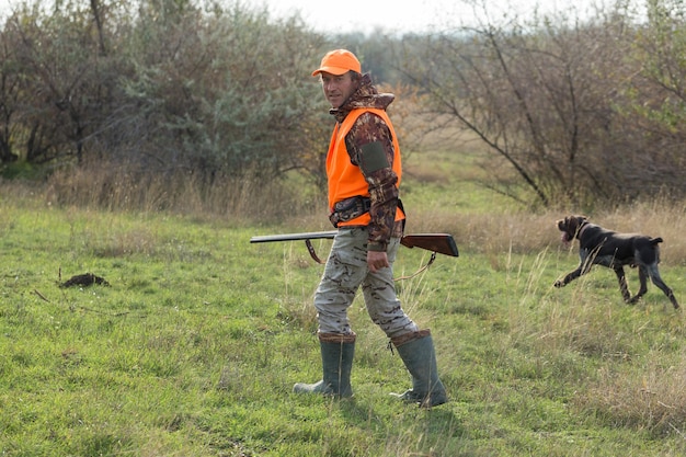 Un uomo con una pistola in mano e un giubbotto arancione a caccia di fagiani in una zona boscosa con tempo nuvoloso Cacciatore con cani in cerca di selvaggina