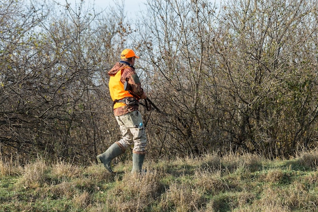 Un uomo con una pistola in mano e un giubbotto arancione a caccia di fagiani in una zona boscosa con tempo nuvoloso Cacciatore con cani in cerca di selvaggina