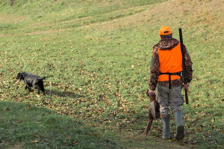Foto un uomo con una pistola in mano e un giubbotto arancione a caccia di un fagiano in una zona boscosa con tempo nuvoloso un cacciatore con un fagiano in mano