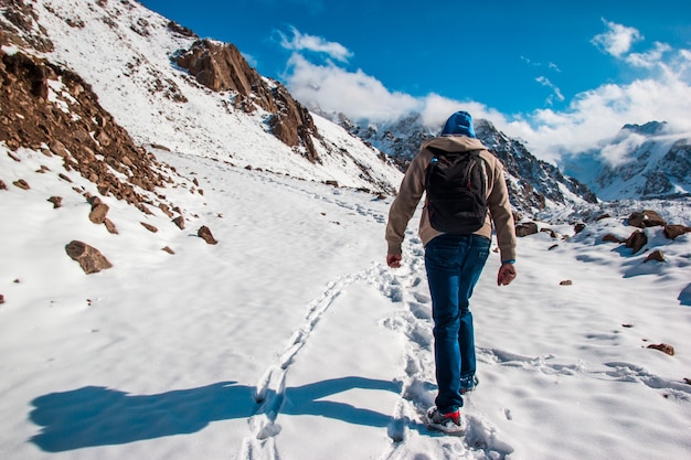 Un uomo con uno zaino fa una scalata in montagna. Segni profondi nella neve.