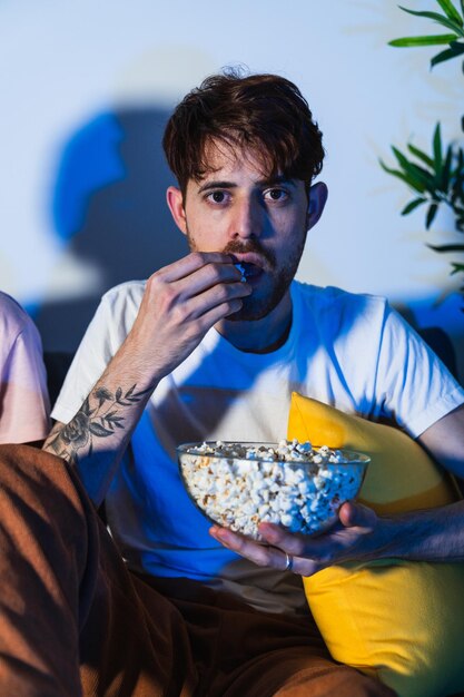 Un uomo concentrato si diverte a mangiare popcorn da solo in una stanza buia che suggerisce un'atmosfera da serata al cinema.