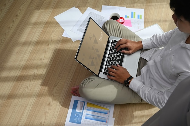 Un uomo concentrato sta lavorando con il laptop e seduto sul pavimento a casa