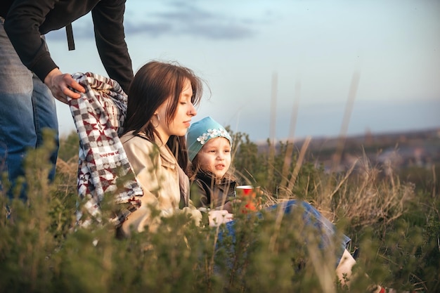 un uomo copre sua moglie e sua figlia con una coperta durante una passeggiata serale nella natura