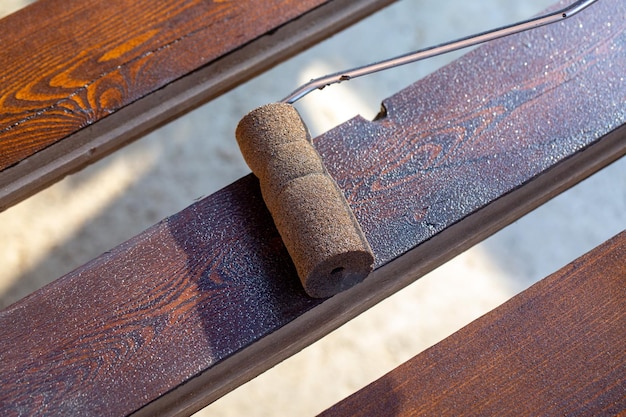 Un uomo copre una tavola di legno con la macchia usando un rullo Falegnameria hobby