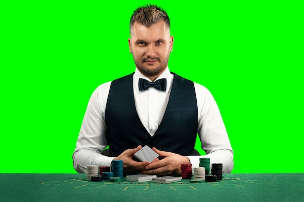 Un uomo croupier si siede a un tavolo con fiches e carte da gioco isolare lo schermo verde