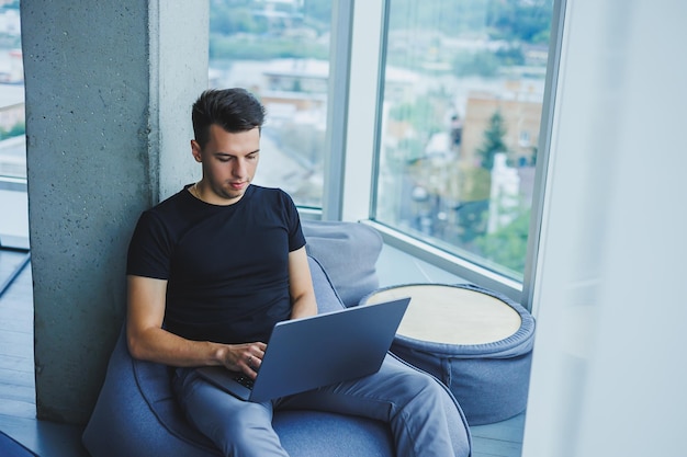 Un uomo d'affari allegro è seduto a lavorare con un computer portatile in ufficio Un uomo d'affari è seduto e sta lavorando su un computer portatile Iniziare la giornata in ufficio