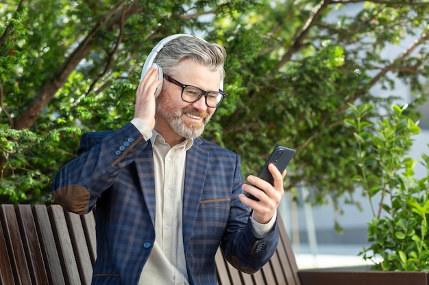 Un uomo d'affari anziano che si diverte a ascoltare musica con le cuffie all'aperto
