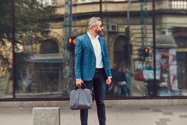 Un uomo d'affari anziano in abito blu con una valigetta che cammina per la città.