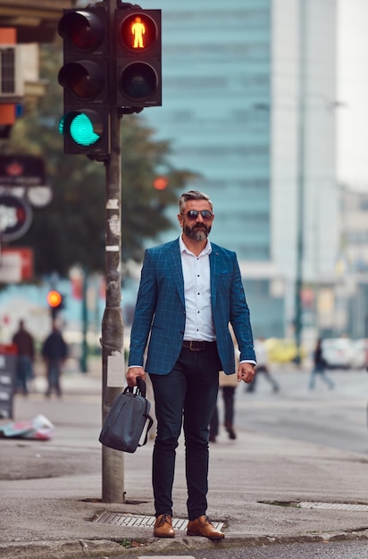 Un uomo d'affari anziano in abito blu con una valigetta che cammina per la città.