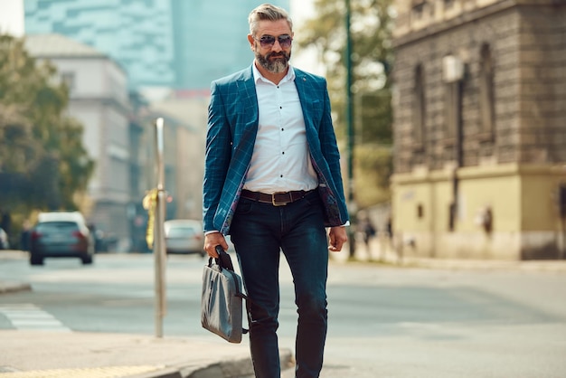 Un uomo d'affari anziano in abito blu con una valigetta che cammina per la città.