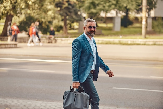 Un uomo d'affari anziano in abito blu con una valigetta che cammina per la città.