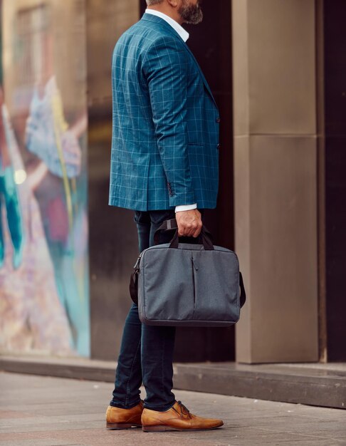 Un uomo d'affari anziano in abito blu con una valigetta che cammina per la città.