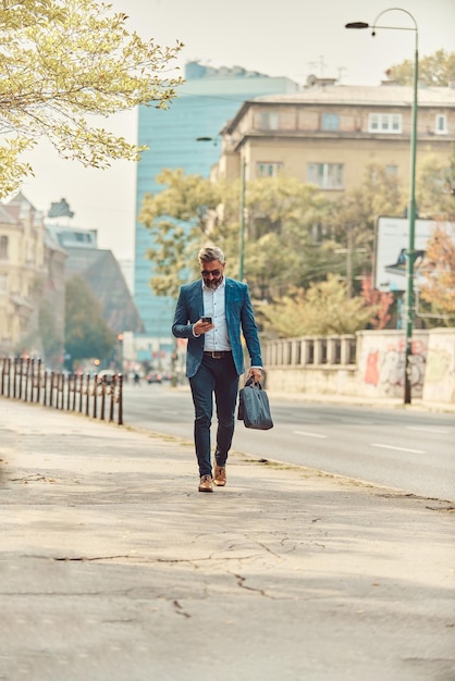 Un uomo d'affari anziano in una tuta blu in un ambiente urbano utilizzando uno smartphone.