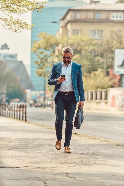 Un uomo d'affari anziano in una tuta blu in un ambiente urbano utilizzando uno smartphone.