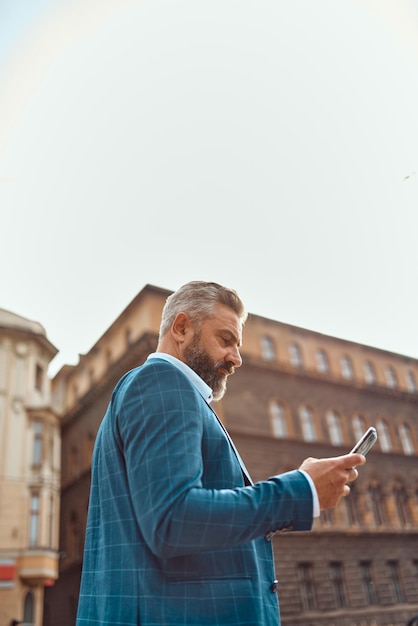 Un uomo d'affari anziano in una tuta blu in un ambiente urbano utilizzando uno smartphone.