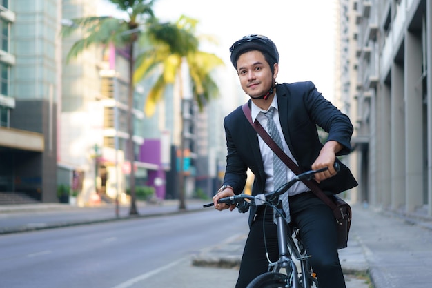 Un uomo d'affari asiatico in giacca e cravatta sta andando in bicicletta per le strade della città per il suo tragitto mattutino per andare al lavoro. Concetto di trasporto ecologico.