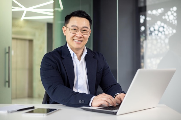 Un uomo d'affari asiatico professionista sorride mentre si occupa del lavoro sul suo portatile in un elegante ambiente ben illuminato