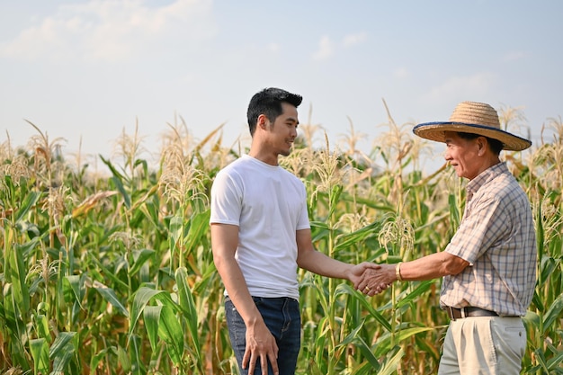 Un uomo d'affari asiatico stringe la mano a un anziano contadino in un campo di grano