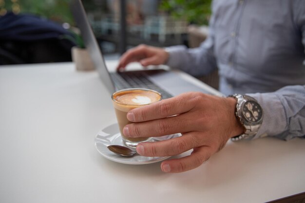 Un uomo d'affari beve il caffè mentre lavora al suo primo piano del computer portatile della sua mano