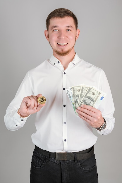 Un uomo d'affari con una camicia bianca tiene una moneta d'oro bitcoin e un fan di banconote da un dollaro di carta nella sua foto verticale della mano