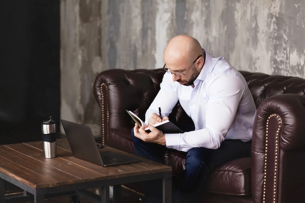 Un uomo d'affari controlla le informazioni in un taccuino mentre lavora con un computer portatile in ufficio