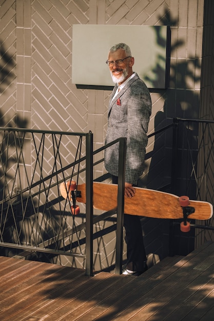 Un uomo d'affari dai capelli grigi con uno skateboard nel distretto degli uffici