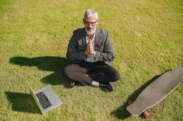 Un uomo d'affari dai capelli grigi seduto sull'erba e meditando