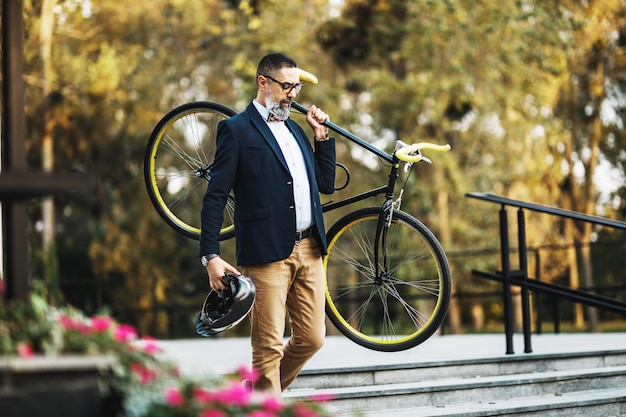 Un uomo d'affari di mezza età va al lavoro in bicicletta e porta una bicicletta in spalla sopra le scale.
