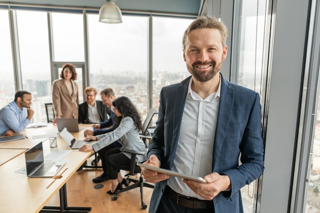 Un uomo d'affari in abito blu si trova in un ufficio moderno con in mano un tablet e sorridendo con fiducia