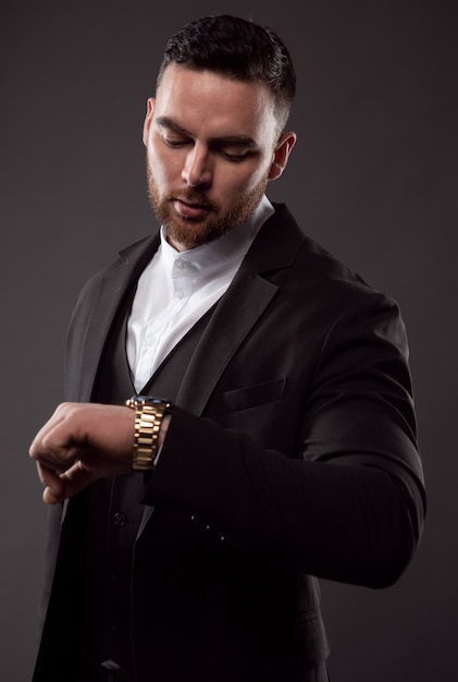 Un uomo d'affari in abito nero guarda l'ora sul suo orologio da polso.