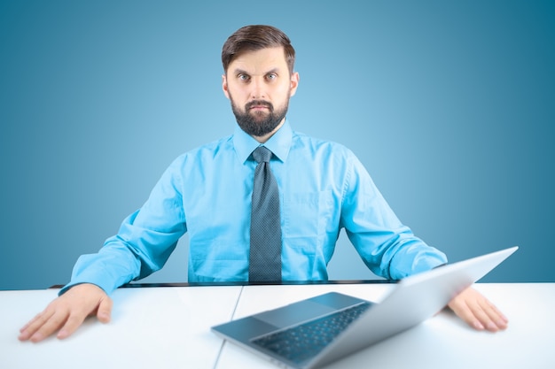 Un uomo d'affari in camicia blu e cravatta incrociò le mani davanti al suo laptop