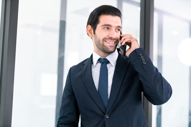Un uomo d'affari in giacca e cravatta è in piedi davanti a una porta a vetri e guarda il suo telefono