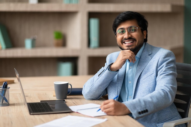 Un uomo d'affari indiano seduto con un sorriso che prende appunti in ufficio