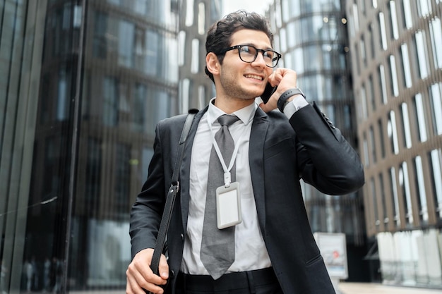 Un uomo d'affari sorridente che parla al telefono all'aperto con edifici moderni sullo sfondo