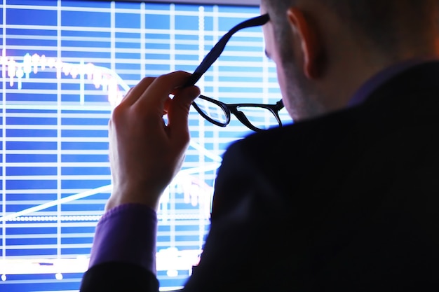 Un uomo d'affari sta guardando un grafico su un monitor. Un broker valuta le tendenze del mercato azionario. Un uomo con gli occhiali davanti a una curva delle dinamiche dell'economia.