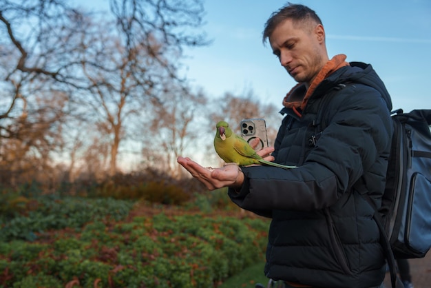 Un uomo dà da mangiare ai pappagalli in un freddo parco londinese durante la stagione invernale