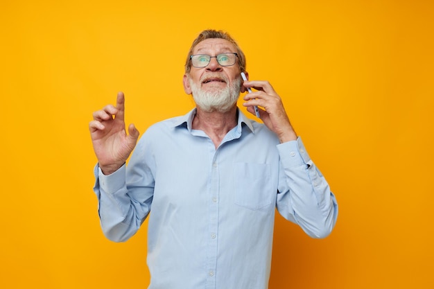 Un uomo dai capelli grigi senior con una camicia blu e occhiali che parla al telefono ha isolato lo sfondo