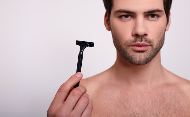 Un uomo di bellezza con una leggera faccia con la barba lunga detiene un rasoio nero