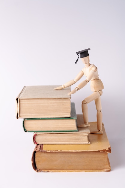 Un uomo di legno con un cappello da studente sale una scala fatta di libri