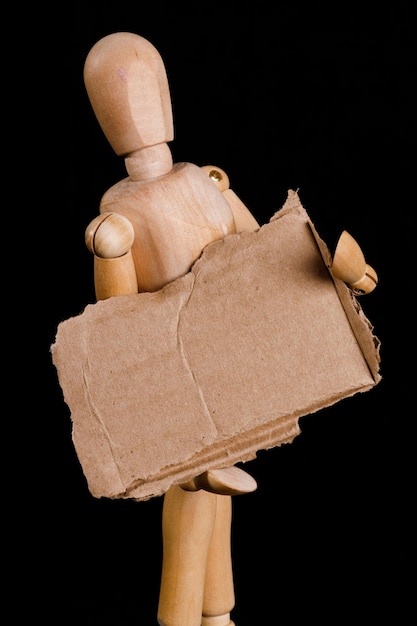 Un uomo di legno tiene un cartello di cartone marrone su sfondo nero Foto di alta qualità