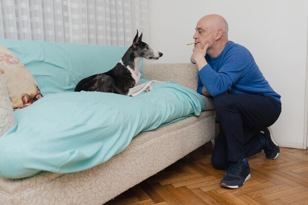 Un uomo di mezza età dà un biscotto al suo cane con la bocca