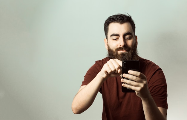 Un uomo di stile giovane hipster con barba e taglio di capelli moderno che sorride mentre guarda il suo schermo del telefono con spazio di copia